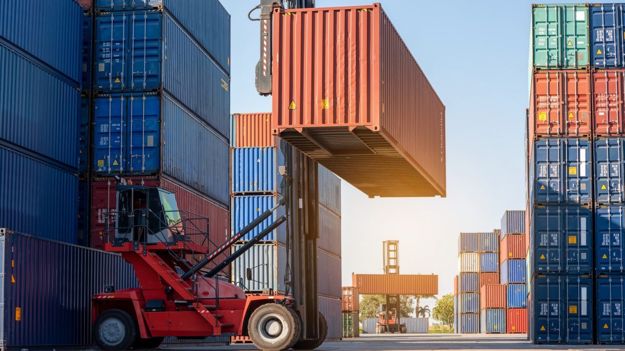 A forklift truck elevates containers, efficiently organizing them within a busy container yard.