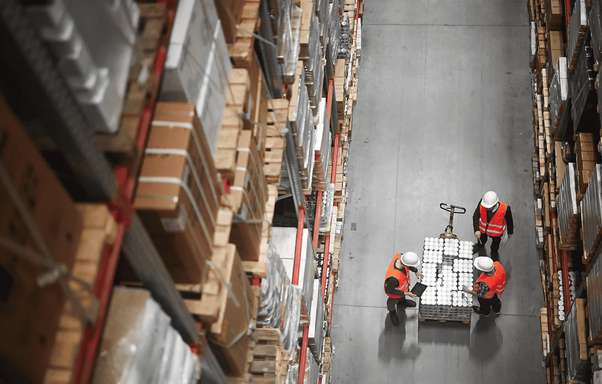 Two workers organizing items in a warehouse aisle, surrounded by shelves filled with various products.