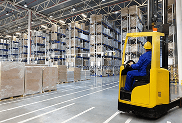 A worker operates a forklift inside a warehouse, efficiently moving goods among the shelves.