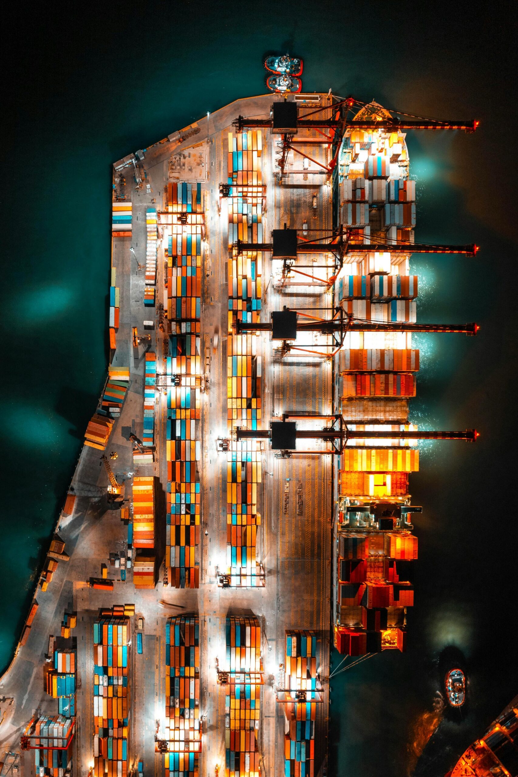 Aerial view of a container port illuminated at night, showcasing rows of containers and docked ships under a dark sky.