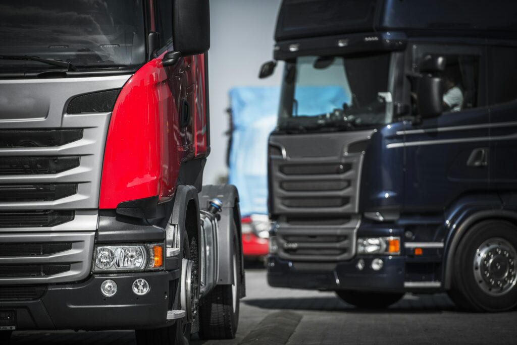 Two large trucks parked side by side in a spacious area, showcasing their size and robust design.