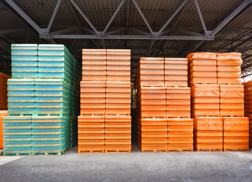 A spacious warehouse filled with numerous stacks of orange and green pallets, showcasing organized storage solutions.